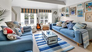 A living room with a blue sofa set, a glass coffee table, and a guitar. - Stunning  villa for 6 guests with WIFI (Fowey)