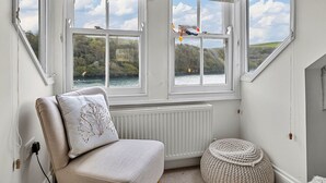 Een kamer met uitzicht op een meer en heuvels, een witte radiator, een witte stoel met een decoratief kussen, en een geweven poef.