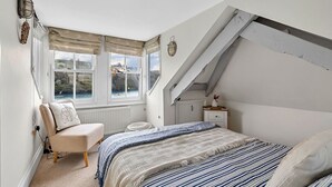 A bedroom with a large bay window, a bed with striped bedding, a chair with a cushion, and a bedside table with a vase. - Stunning  villa for 6 guests with WIFI (Fowey)