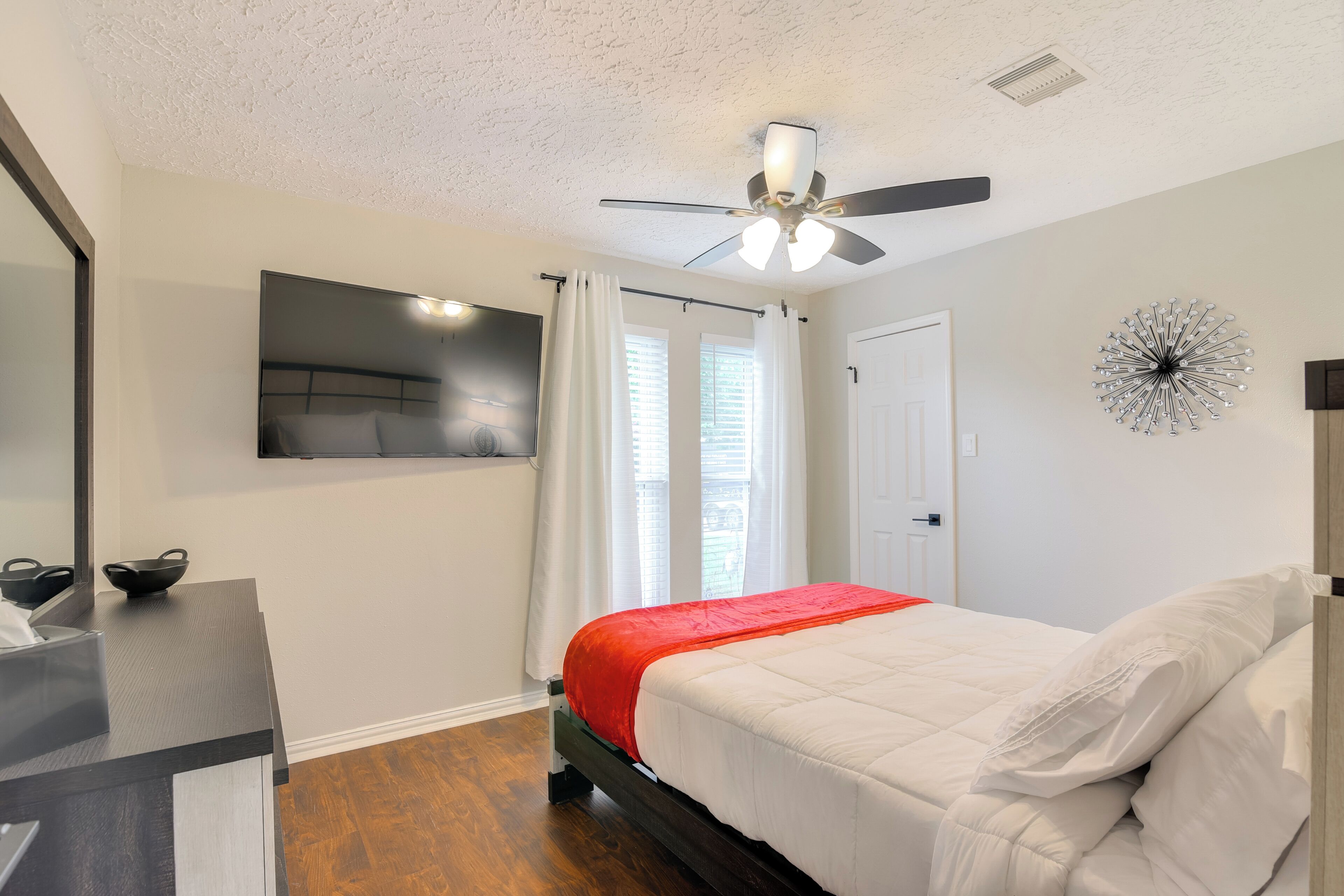 A bedroom with a bed, a ceiling fan, a mounted TV, and a window with curtains.