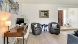 A modern living room with a desk, two armchairs, a TV, and a painting on the wall.