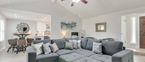 A modern living room with a sectional sofa, a dining area with a round table, and a ceiling fan.