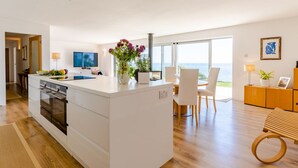 A modern kitchen with a central island, dining area with chairs, and a view of the sea. - Stunning  villa for 6 guests with WIFI, TV and pets allowed (Saltash)