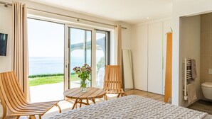 A bedroom with a large bed, a wooden chair, a small table with a vase, and a view of the sea through a sliding door. - Stunning  villa for 6 guests with WIFI, TV and pets allowed (Saltash)