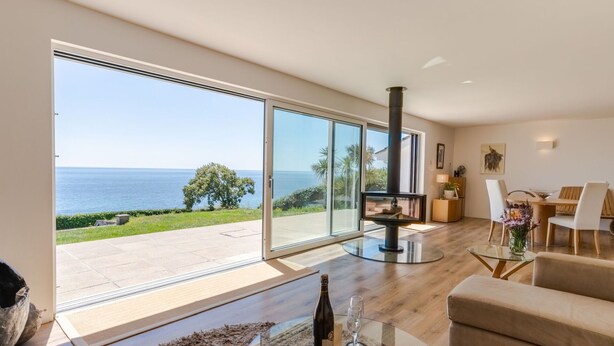 A modern living room with a large glass door leading to a balcony overlooking the sea. - Stunning  villa for 6 guests with WIFI, TV and pets allowed (Saltash)