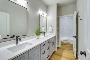 A modern bathroom with a large mirror, two sinks, a plant, and a bathtub.