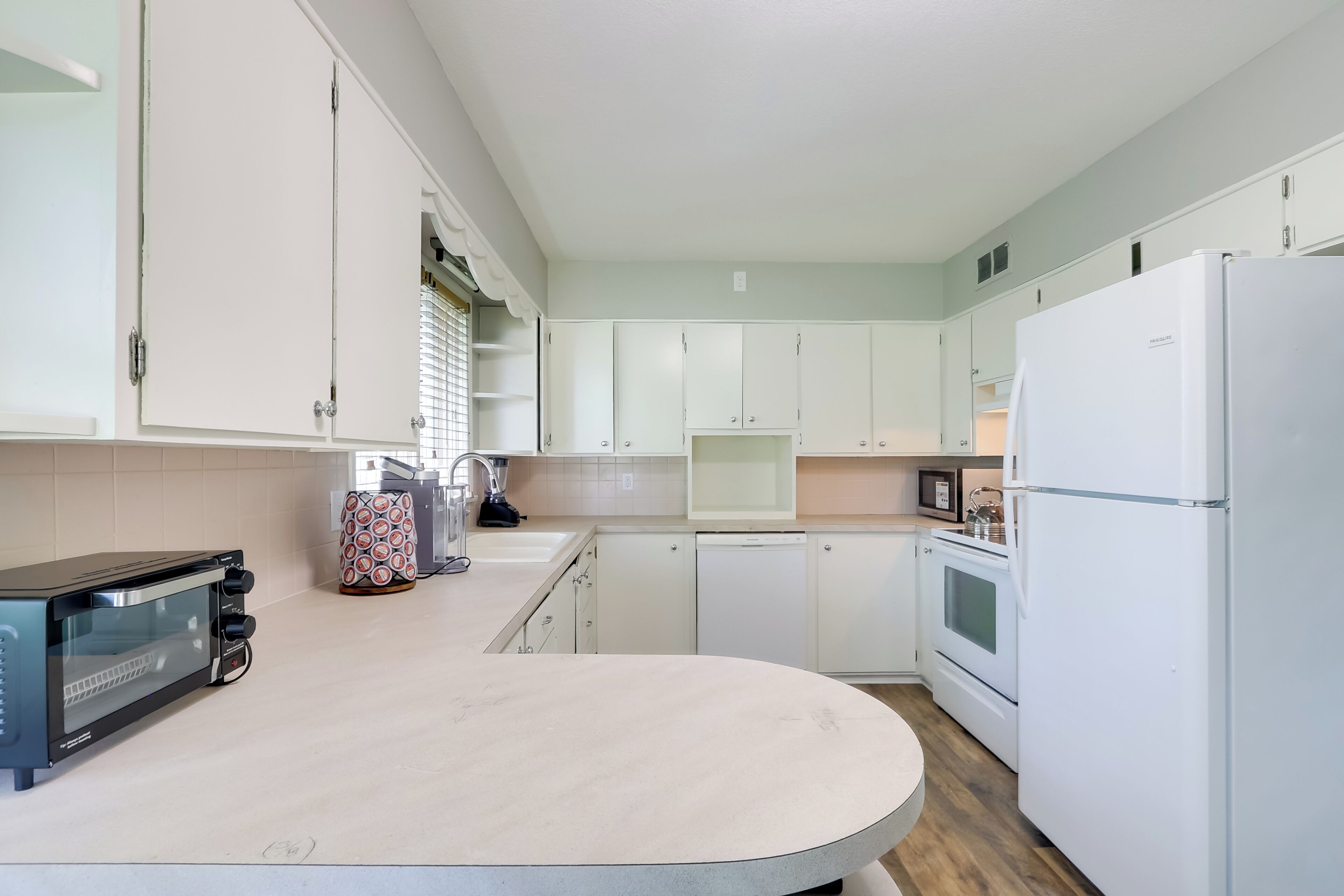 A modern kitchen with white cabinets, a built-in oven, a refrigerator, and a toaster.