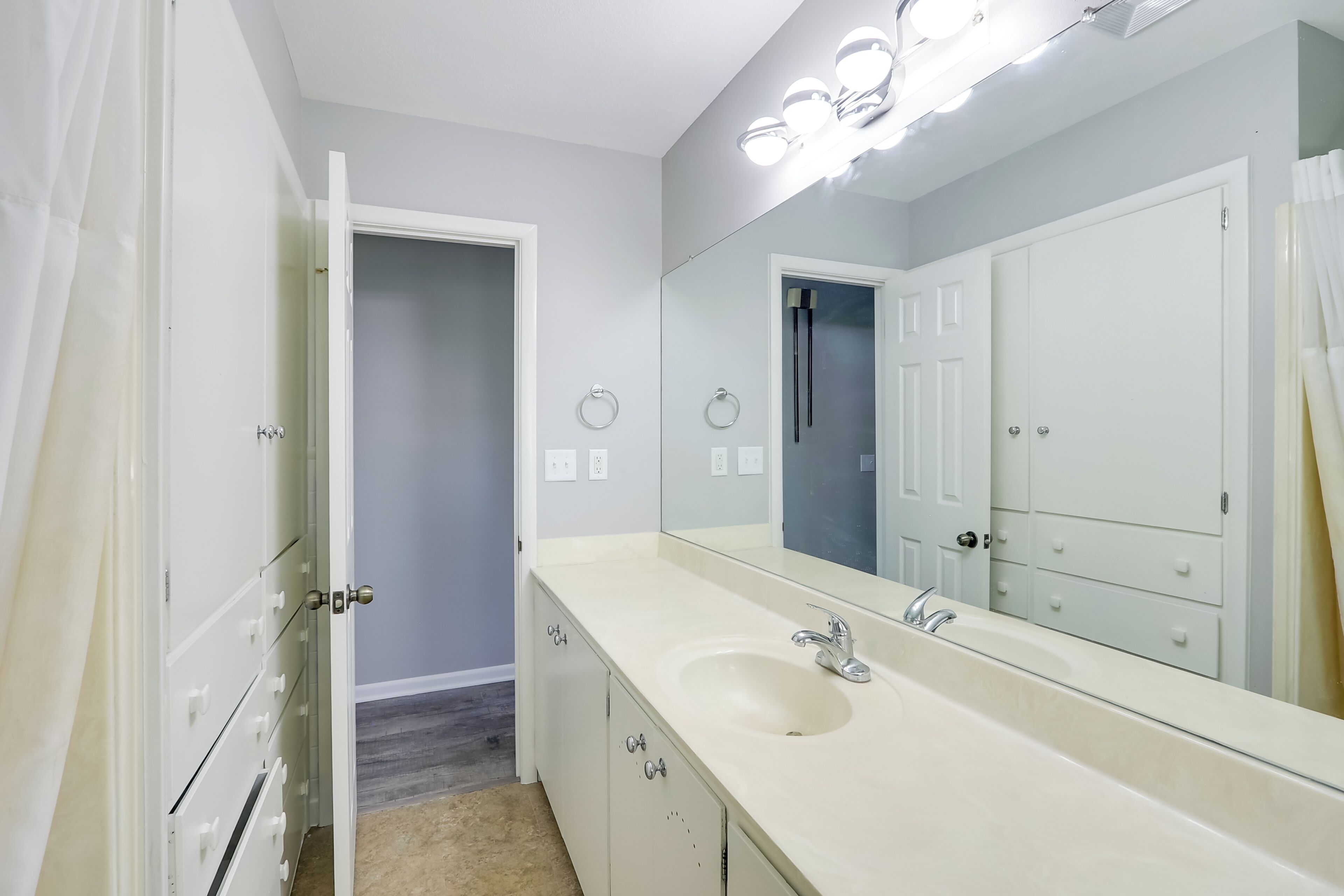 A bathroom with a large mirror, a sink, and a door leading to another room.