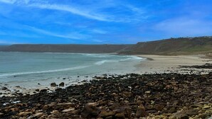 Une plage rocheuse offrant une vue dégagée sur l’océan et une colline lointaine.