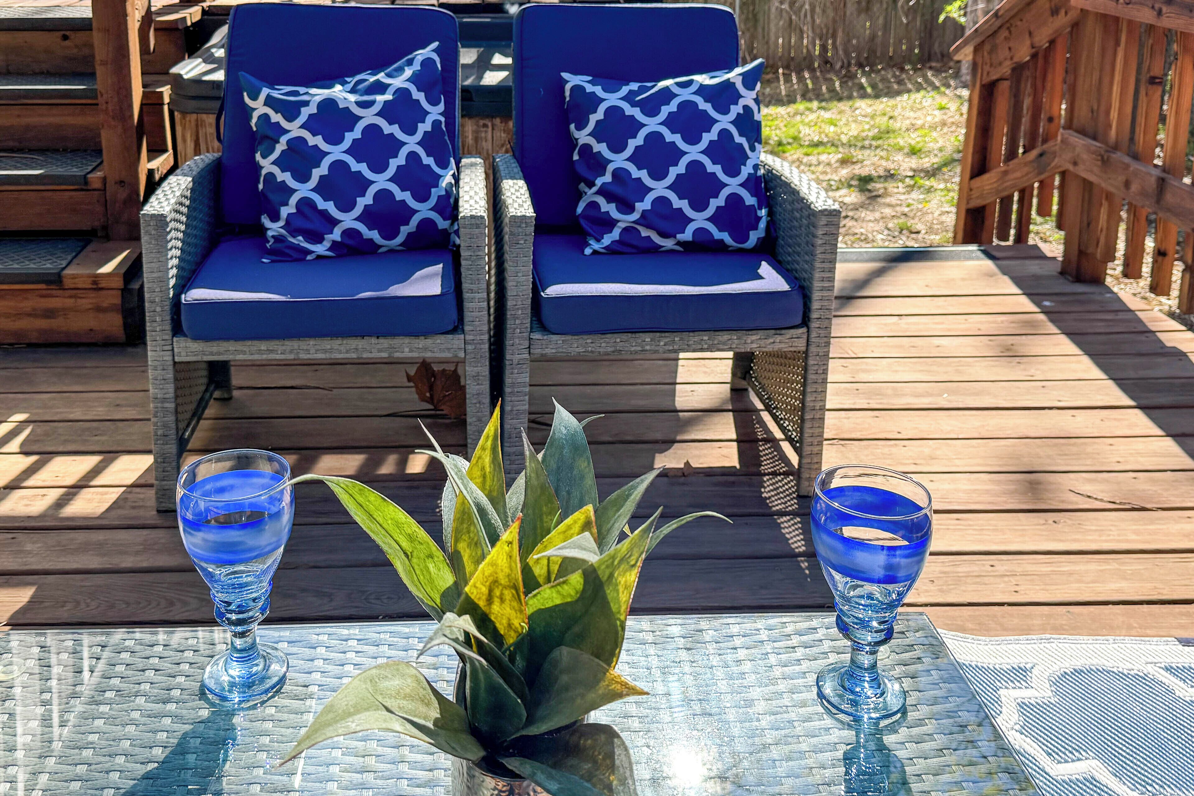 A deck with wicker chairs and a table, a potted plant, and two glasses of blue liquid.