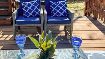 A deck with wicker chairs and a table, a potted plant, and two glasses of blue liquid.