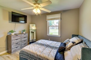 A bedroom with a bed, dresser, ceiling fan, TV, window, and a view of the outside.