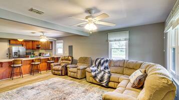 A spacious living room with a large beige sectional sofa, a kitchen area with wooden cabinets, and a ceiling fan.