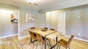 Un comedor con una mesa de madera y seis sillas, un tapete estampado y obras de arte en las paredes.
