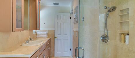 A bathroom with a glass-enclosed shower, a sink, and a mirror.