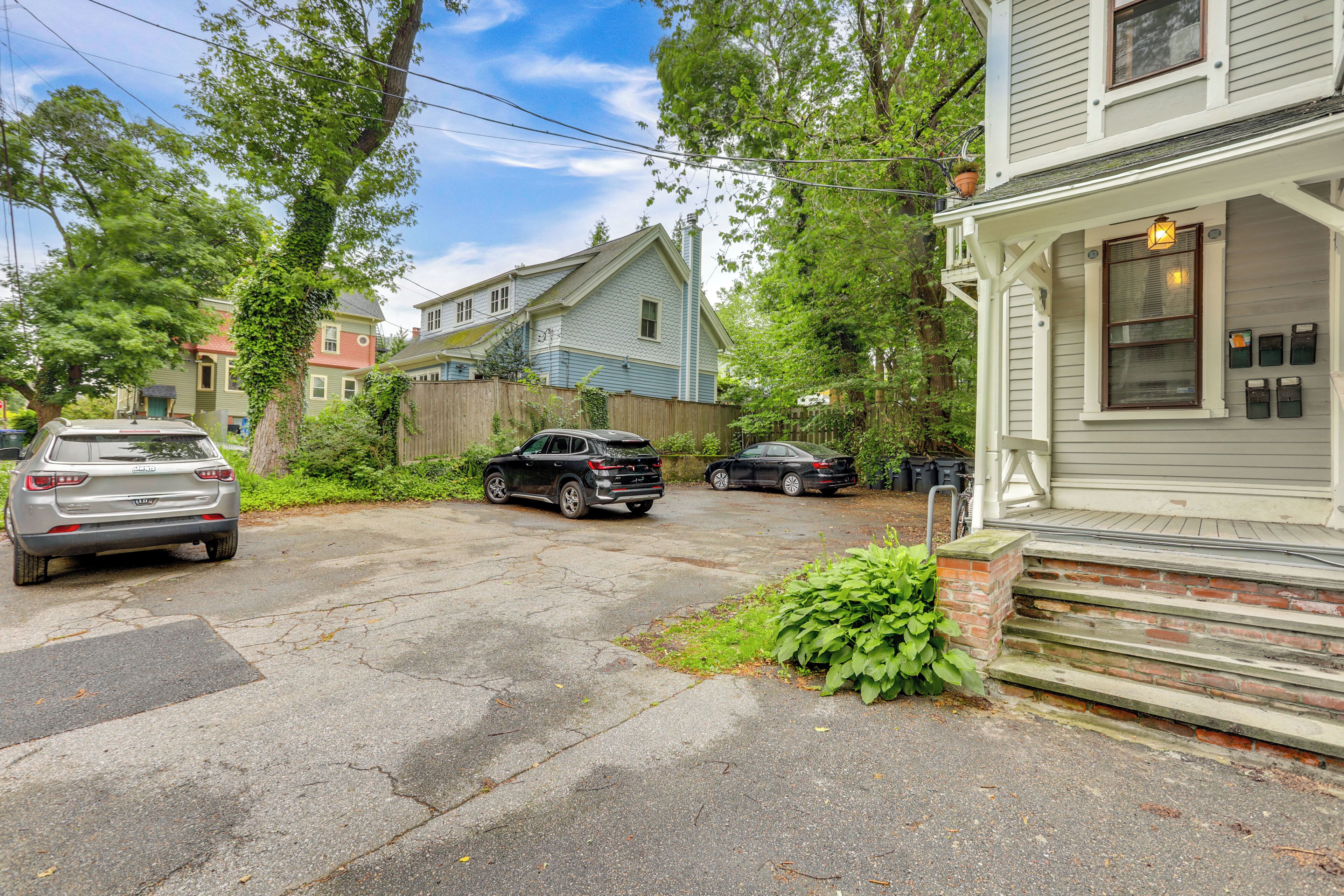 A residential street with houses, parked cars, and a brick staircase leading to a porch.