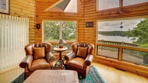 A cozy cabin interior with two leather armchairs, a small table, and a view of a lake through large windows. - Decks & Views: Spacious Cabin Near Table Rock Lake (Shell Knob)