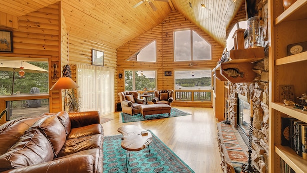 A spacious wooden cabin with a high ceiling, a fireplace, leather furniture, and large windows offering scenic views. - Decks & Views: Spacious Cabin Near Table Rock Lake (Shell Knob)