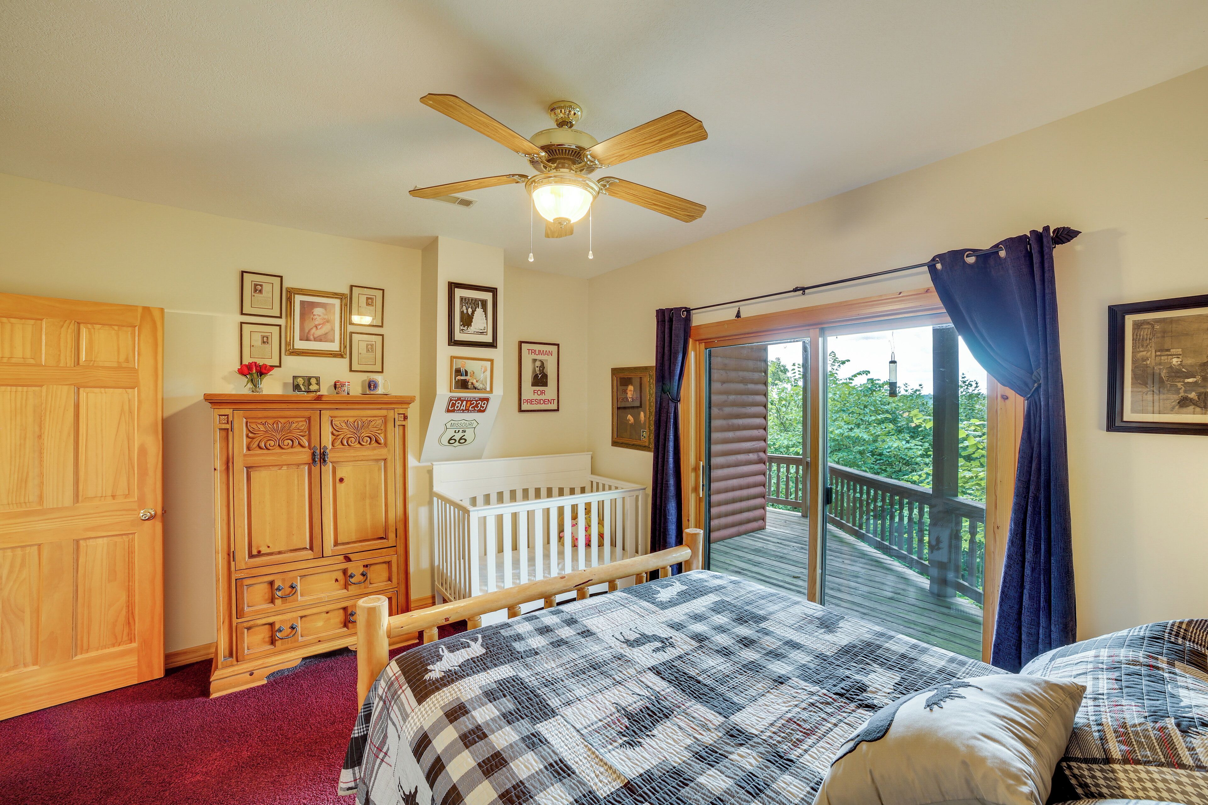 Une chambre à coucher avec un grand lit, un berceau, une armoire en bois et un balcon donnant sur la forêt.