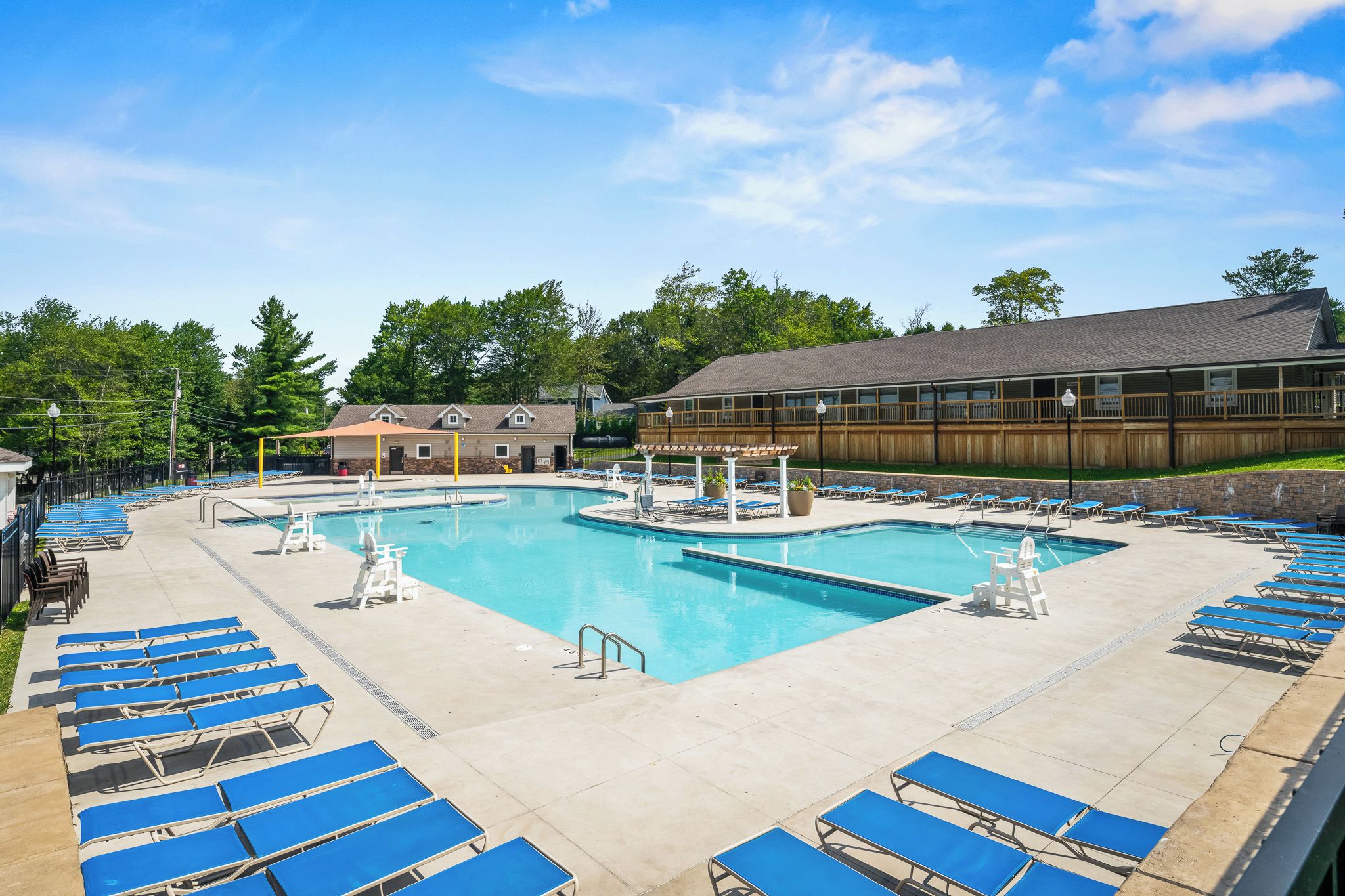 A large outdoor swimming pool with multiple lanes, surrounded by blue lounge chairs and a covered area with a wooden deck.
