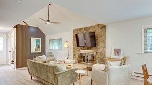 A modern living room with a stone fireplace, a flat-screen TV, and a ceiling fan. - Lake Access at Family-friendly Home in Tobyhanna (Tobyhanna)