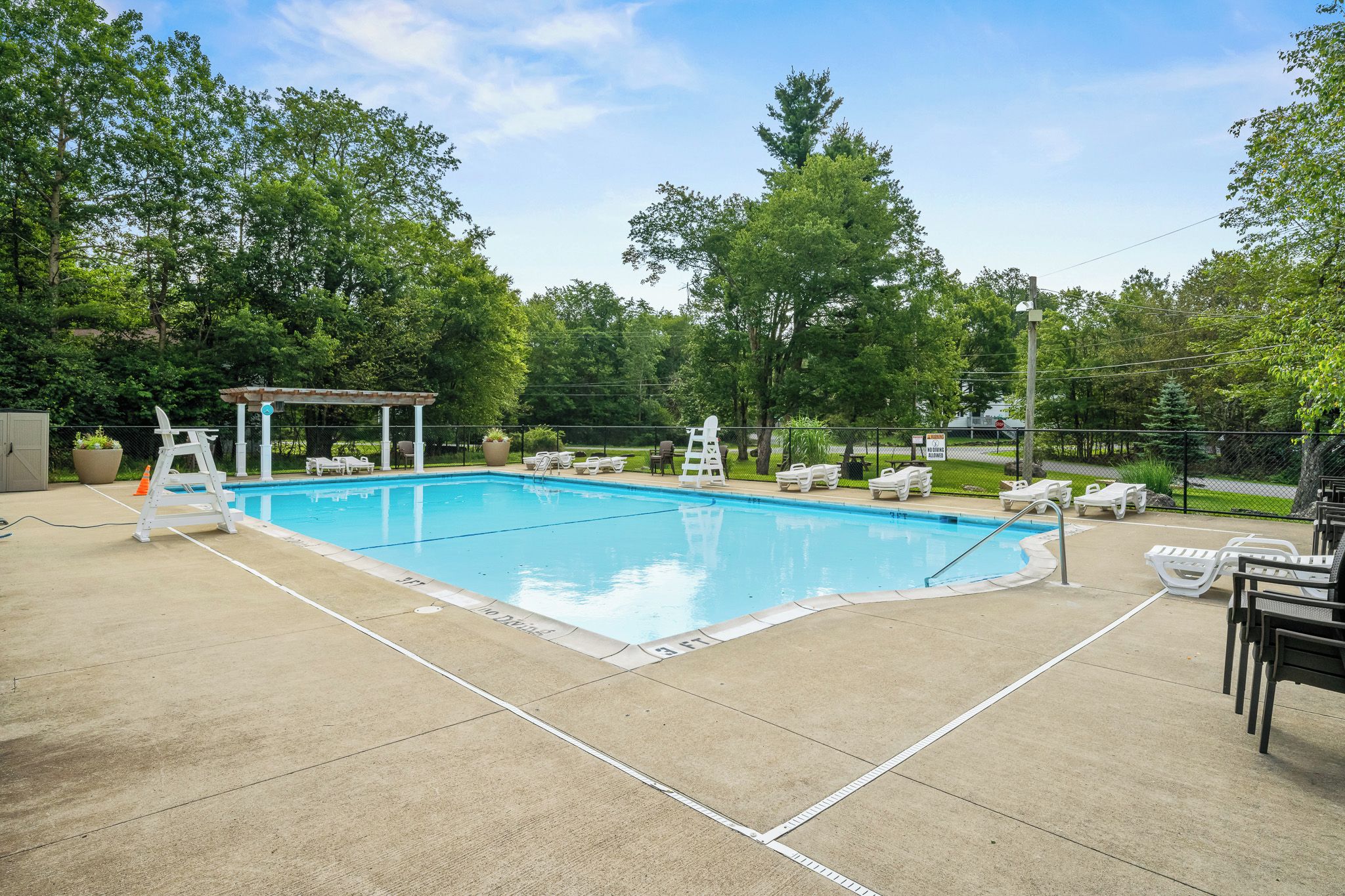 Una piscina rectangular con un deck de concreto, rodeada de sillas de descanso blancas y una zona de estar cubierta.