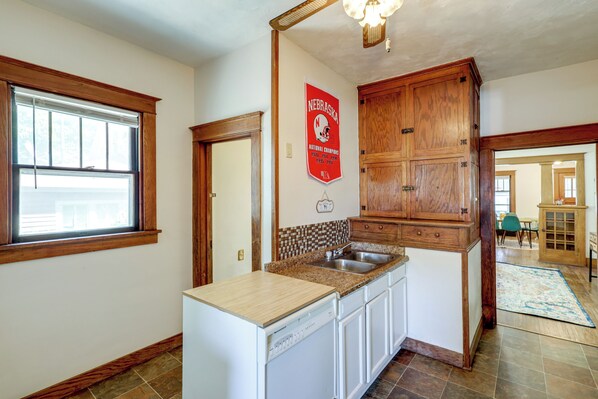A kitchen with wooden cabinets, a built-in dishwasher, and a window with blinds.