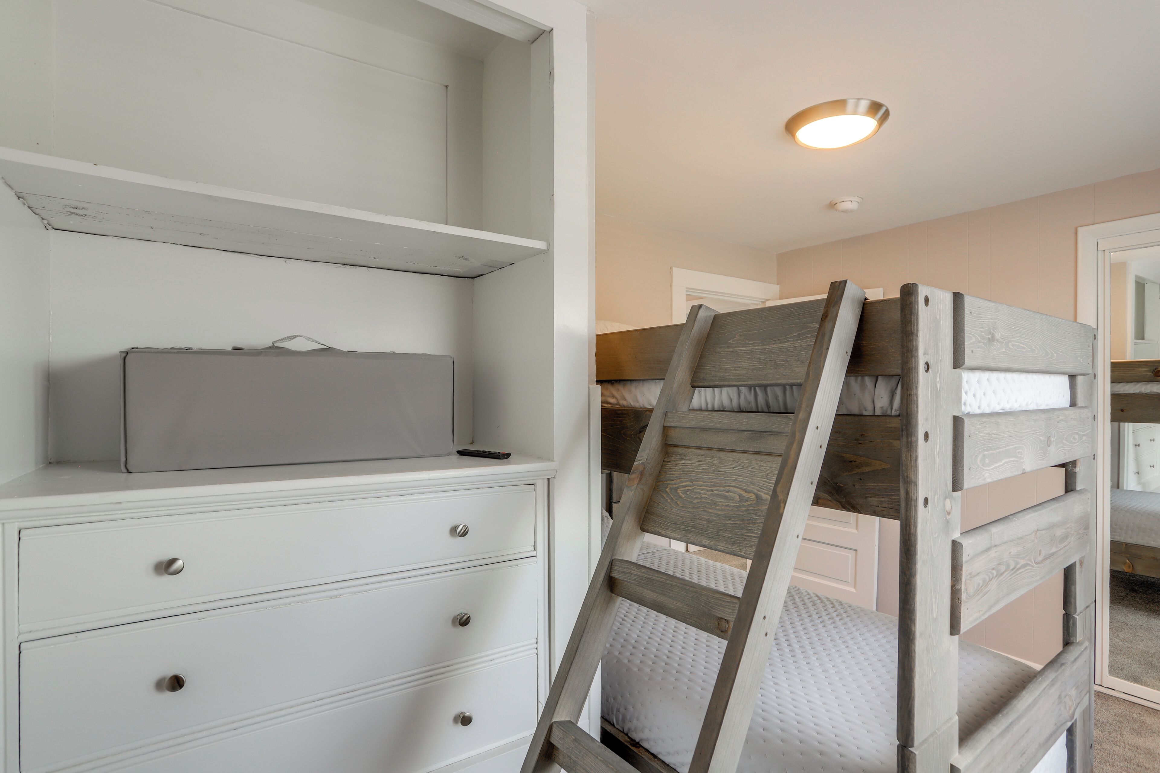 A bedroom with a bunk bed, a white dresser with drawers, and a small bedside table.