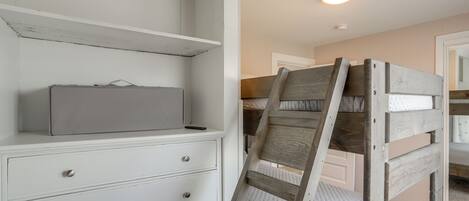 A bedroom with a bunk bed, a white dresser with drawers, and a small bedside table.