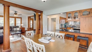 A spacious dining area with a wooden table and white chairs, a kitchen with wooden cabinets, and a living room with a sofa and coffee table.