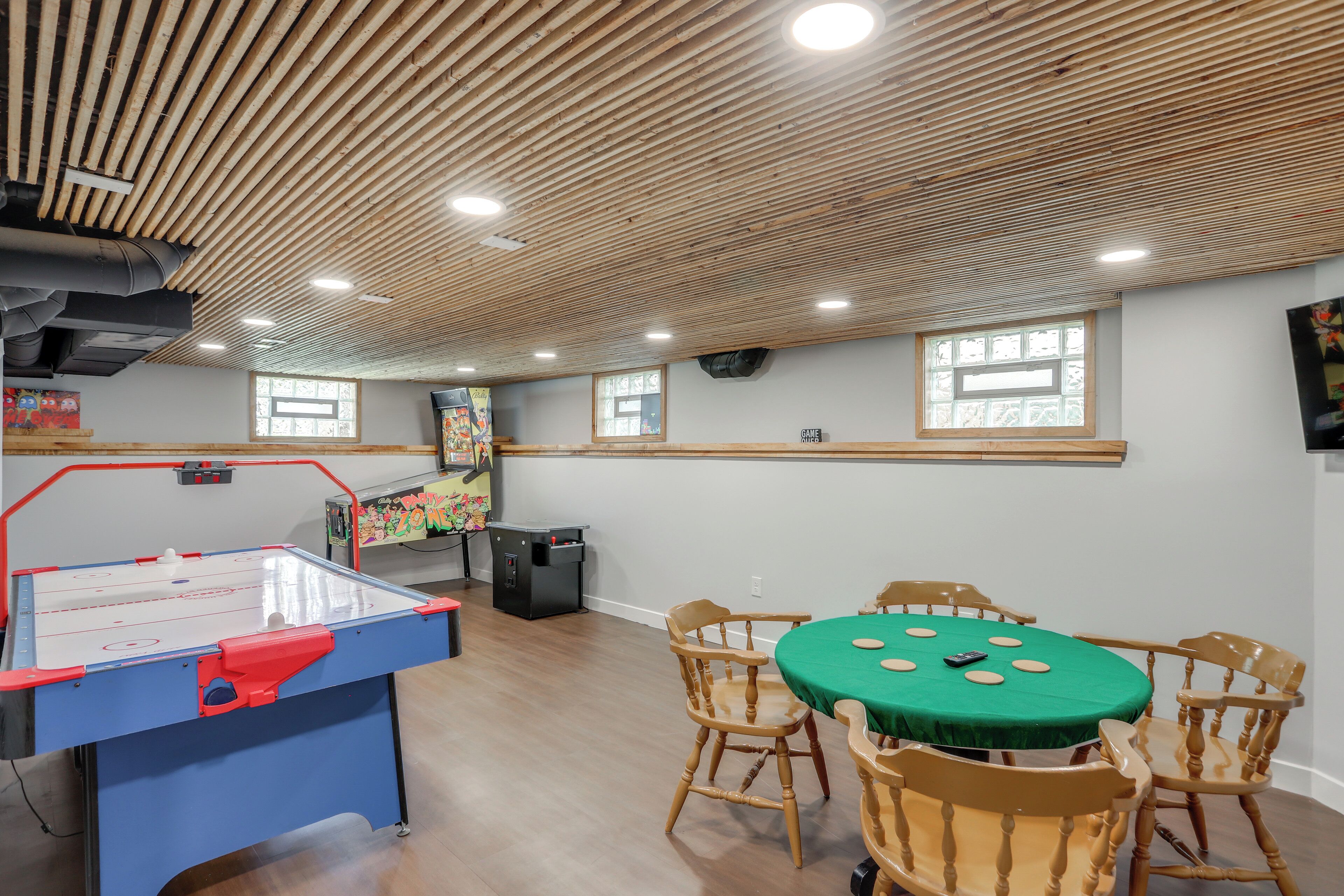 A room with a foosball table, a table with a green tablecloth, wooden chairs, and a window with a view.