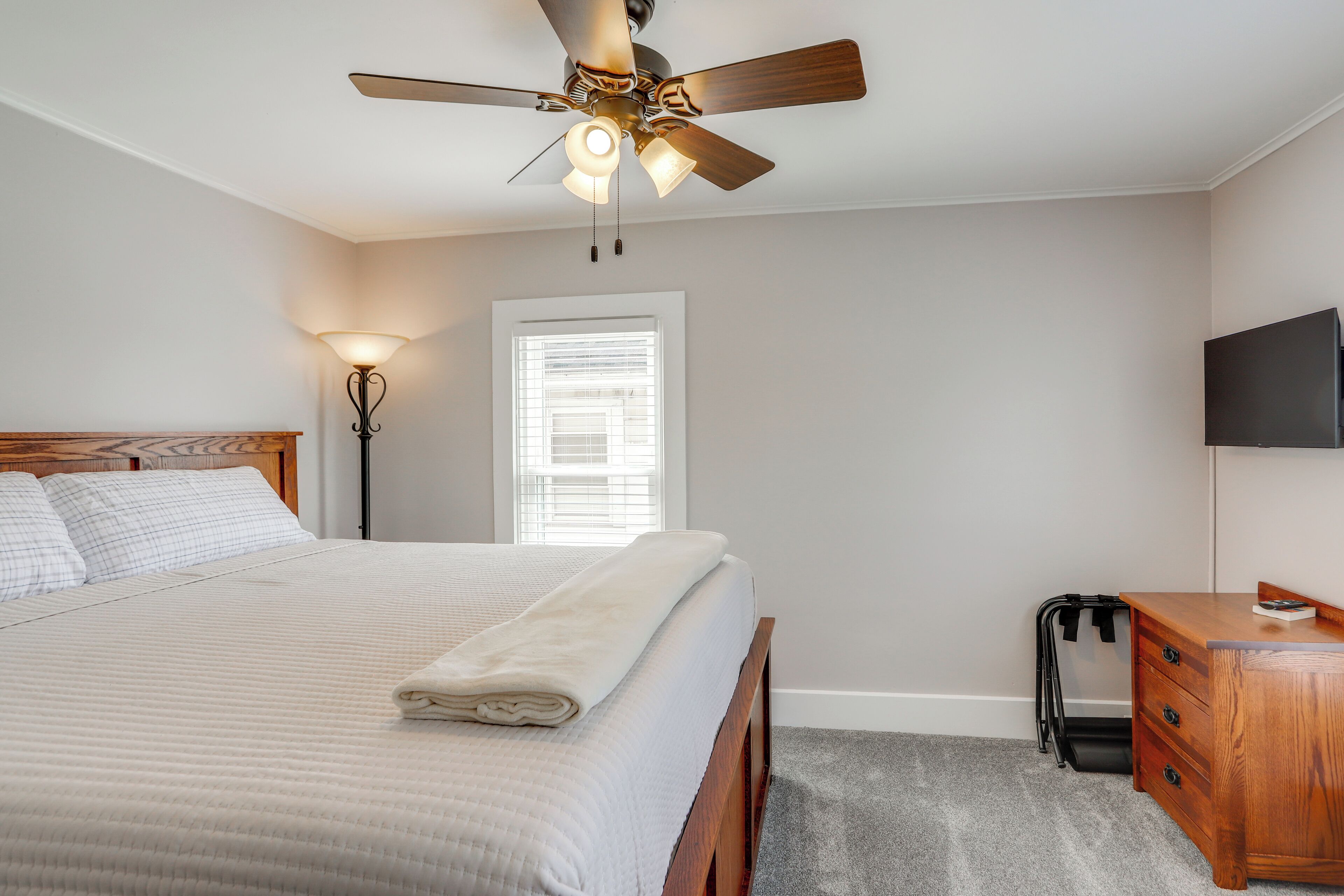 A bedroom with a bed, a ceiling fan, a desk, and a TV.