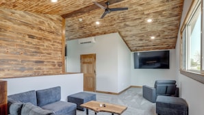A modern living room with a wooden ceiling, grey sofas, a wooden coffee table, and a flat-screen TV.