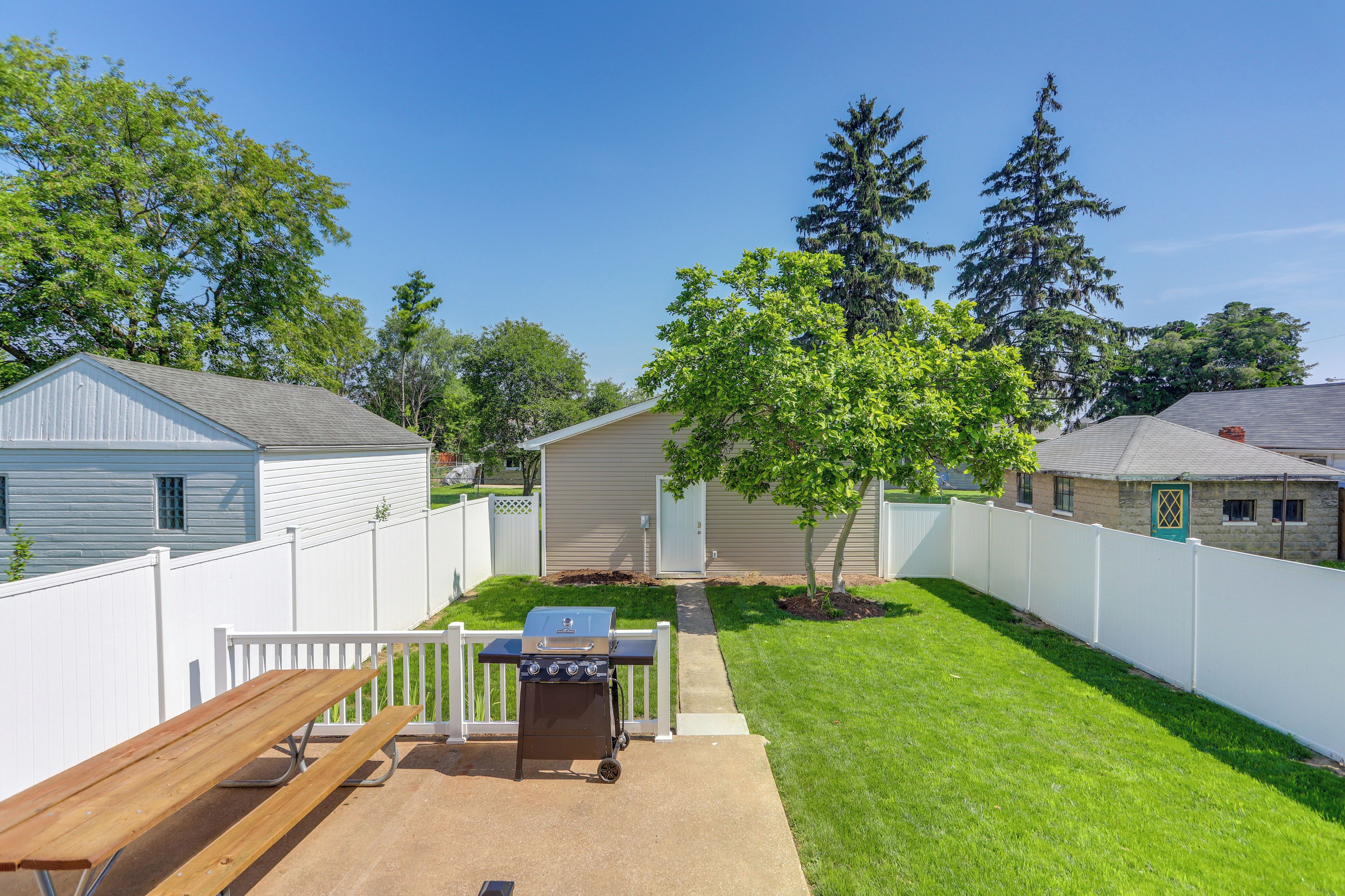 A backyard with a barbecue grill, a wooden bench, and a white fence.