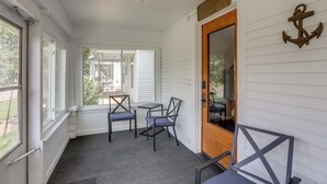 A covered porch with a table and chairs, a wooden door, and a view of the outdoors.