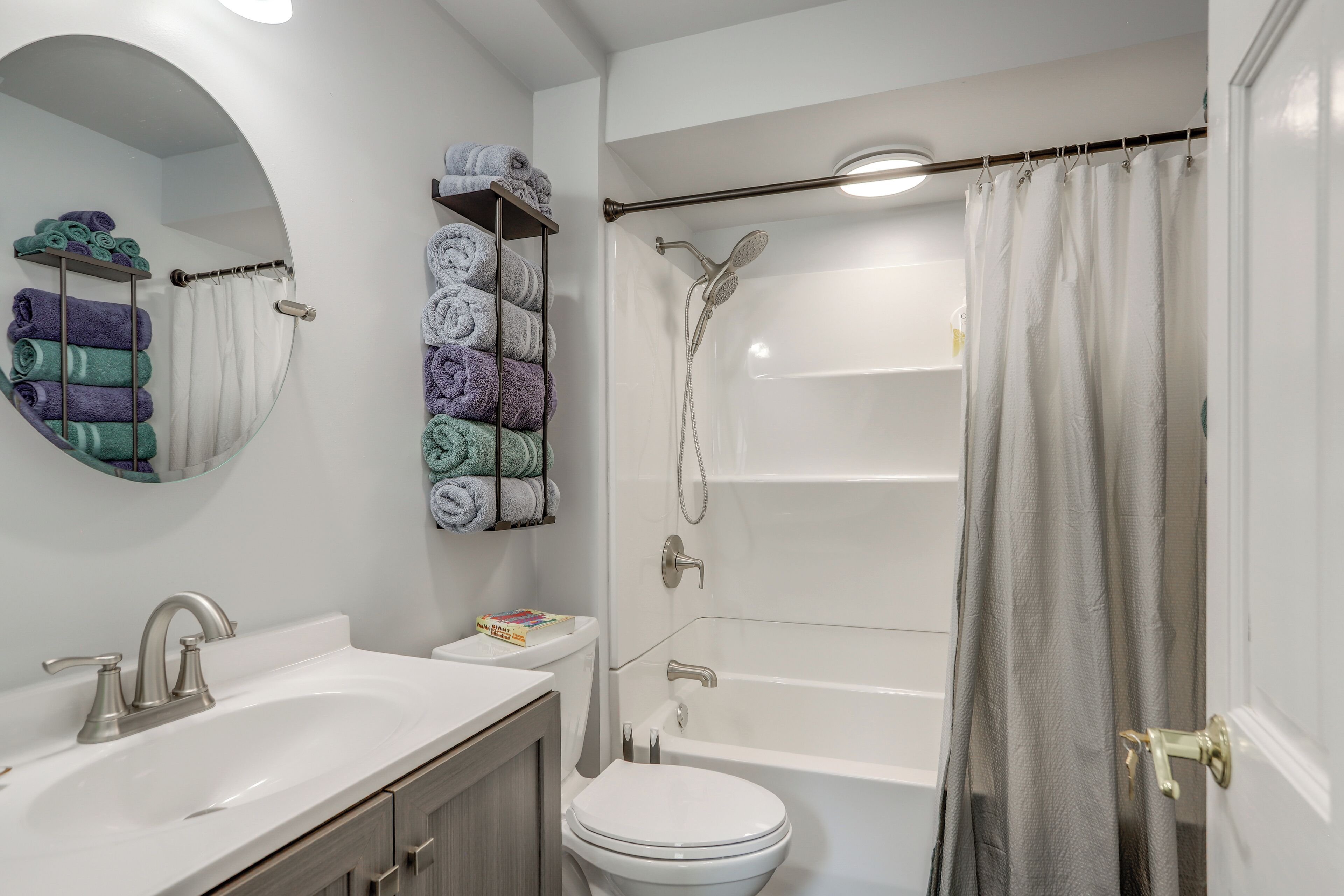 A bathroom with a white sink, toilet, and bathtub. There are towels on a rack and a shower curtain.