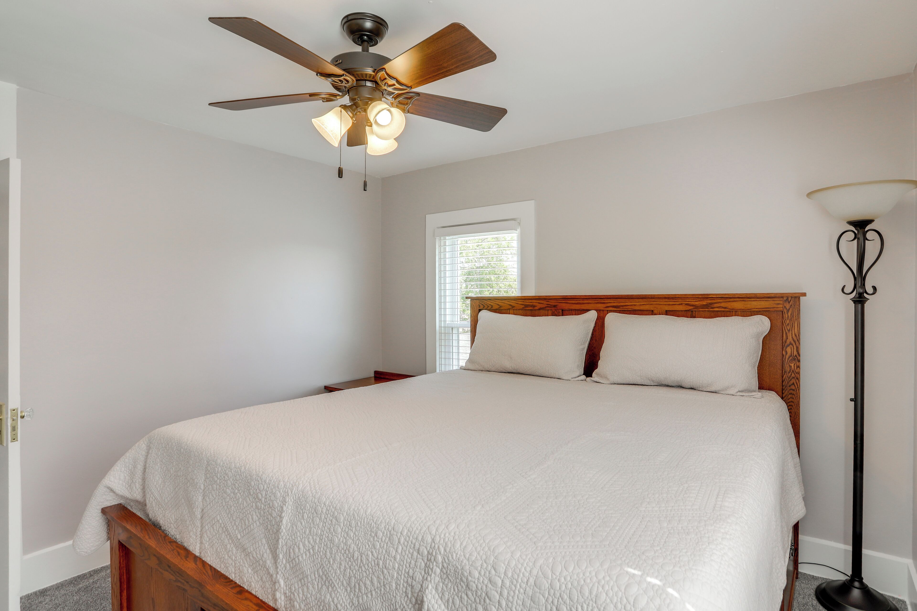 A bedroom with a wooden bed, a ceiling fan, a bedside table, and a floor lamp.