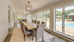 A spacious dining area with a large wooden table and comfortable chairs, large windows offering a view of a swimming pool and outdoor area. - Pool, Lake & Patio: Sweeping De Soto Estate (De Soto)