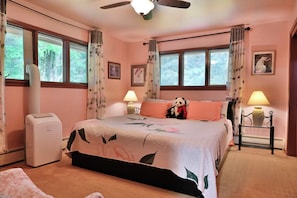 A bedroom with a bed, two bedside lamps, a heater, a window with curtains, and a ceiling fan.