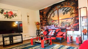 A living room with a flat-screen TV, a sofa with red cushions, a bookshelf, and a large window with a view. - Private 5-acre Lake: Pet-friendly Grove City Home (Grove City)