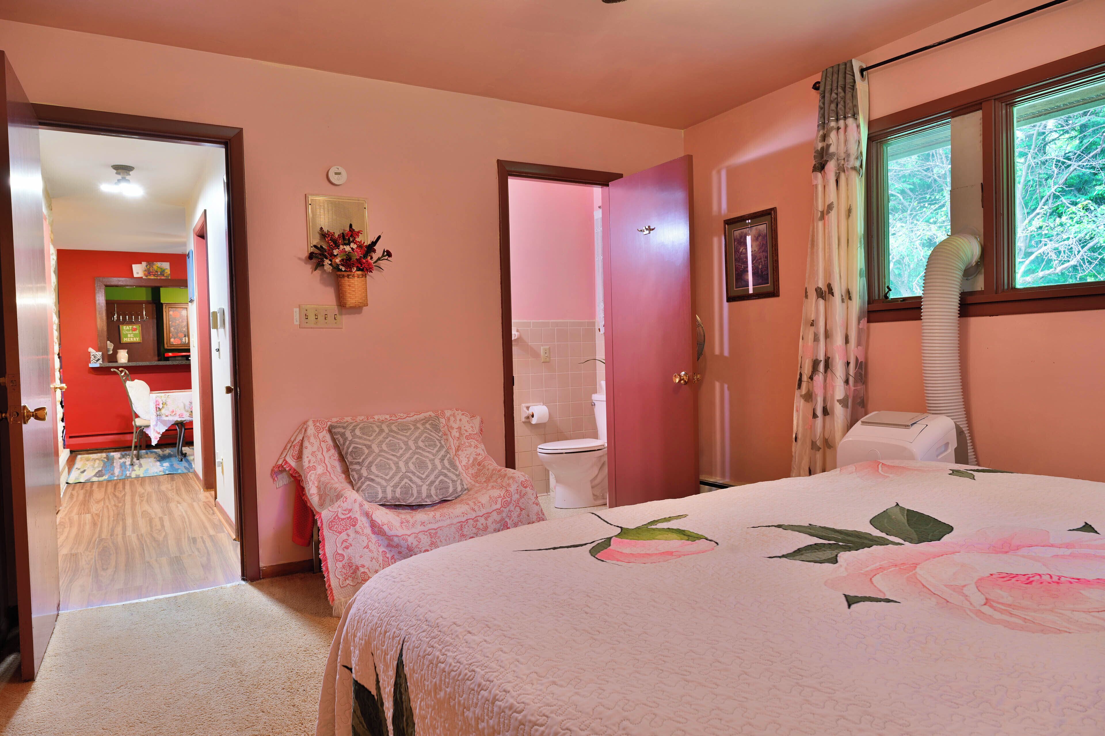 A bedroom with a bed, a chair, a toilet, and a window with a view.