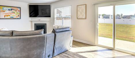 A modern living room with a sectional sofa, a flat-screen TV, a fireplace, and a sliding glass door to a backyard.