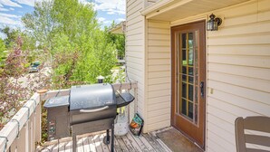 Una terraza de madera con una parrilla, una puerta y una silla.
