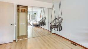 Una habitación con puerta de vidrio corredera que da a un comedor, un sillón colgante y una cama con cabecera blanca.