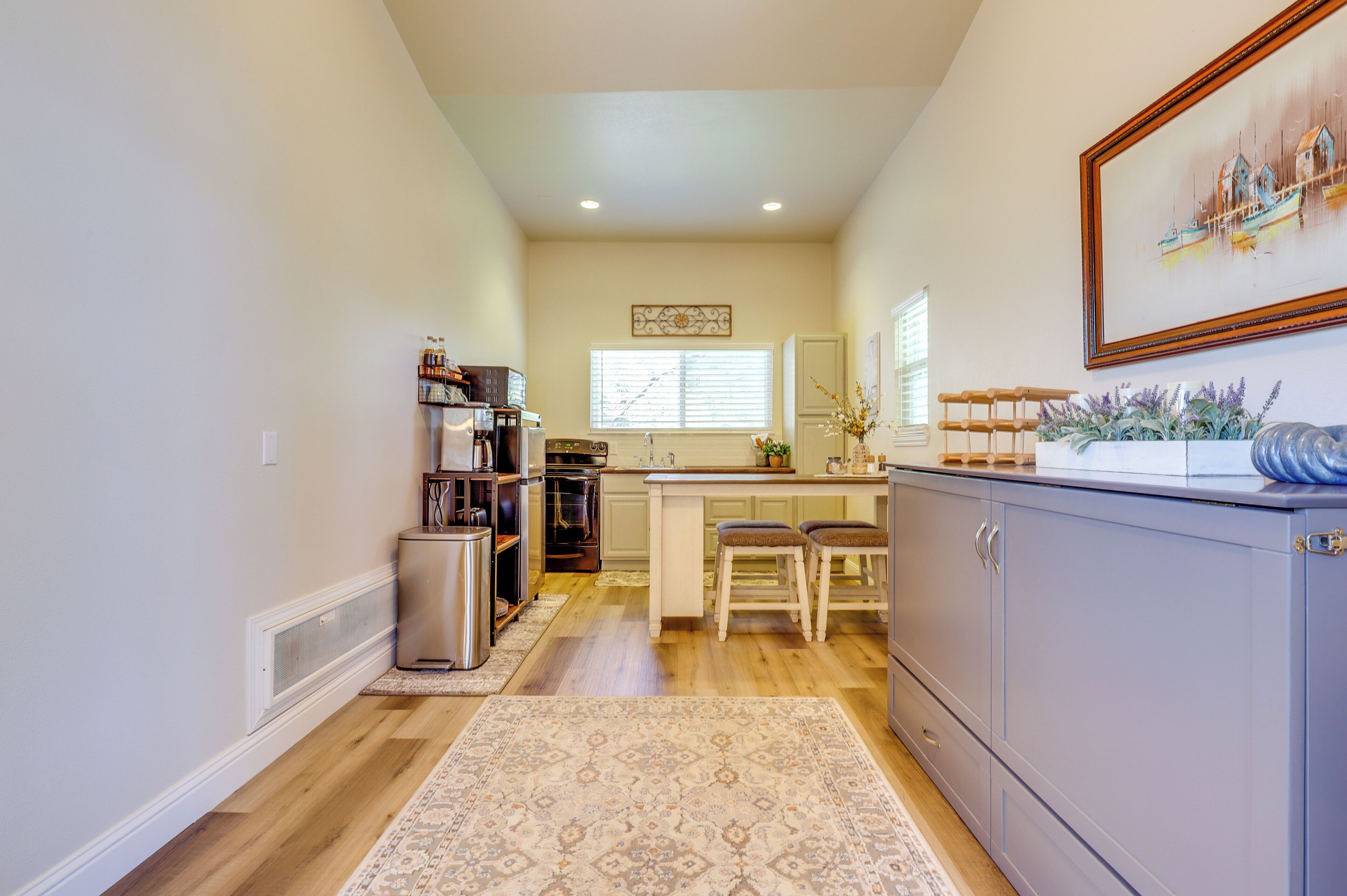 A kitchen with wooden flooring, a central island with stools, a sink, and cabinets.
