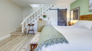 Un dormitorio con cama, escritorio, silla, escalera y espejo.