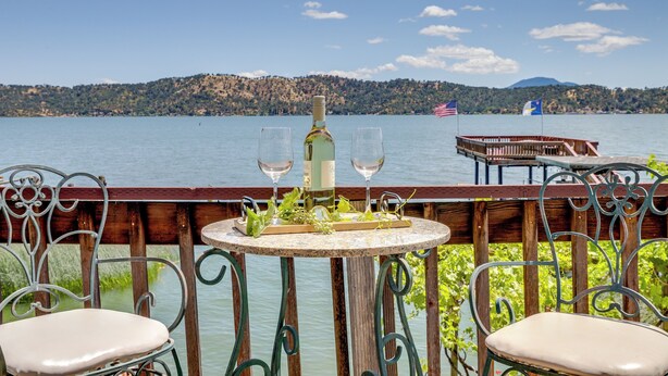 Una mesa con una botella y vasos, con vista a un lago con barcos y banderas.