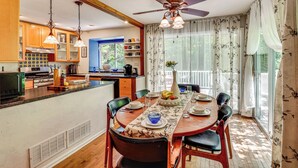 Une cuisine avec des meubles en bois, une table à manger pour quatre personnes et un ventilateur de plafond.