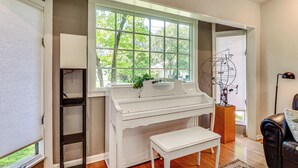 Une pièce avec un piano, un banc, une fenêtre donnant sur des arbres et une sculpture.