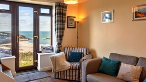 A living room with a view of the beach, a striped armchair, a sofa, and a floor lamp. - Wonderful  villa for 3 people with WIFI and pets allowed (Penzance)